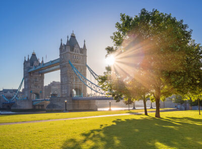 London, UK - Iconic Tower Bridge at sunrise in the morning with sunlight, tree, blue sky and green grass
